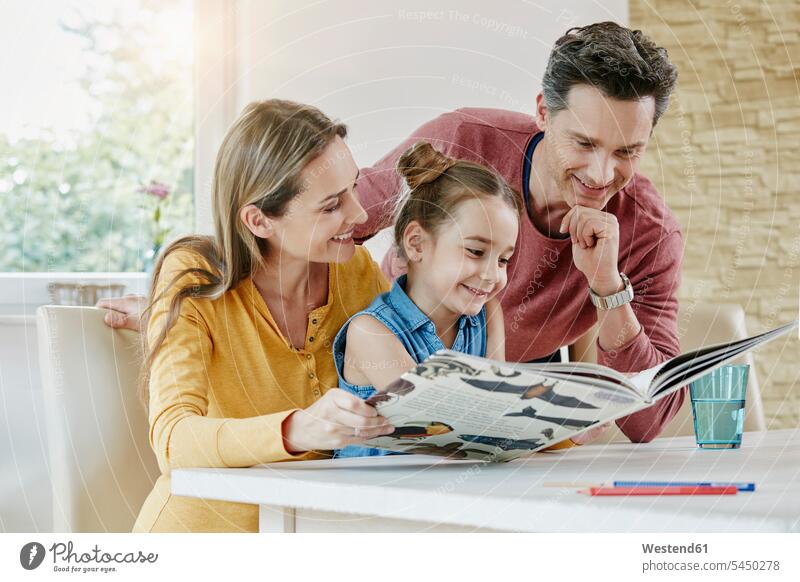 Glückliche Familie zu Hause schaut Bilderbuch an Buch Bücher ansehen glücklich glücklich sein glücklichsein lesen Lektüre Tochter Töchter Familien lächeln