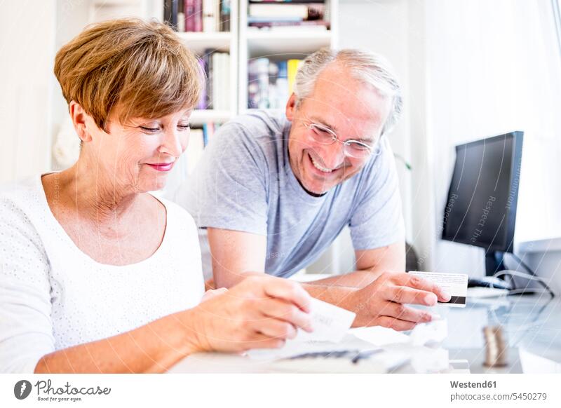 Älteres Ehepaar am Schreibtisch beim Bezahlen von Rechnungen Paar Pärchen Paare Partnerschaft lächeln Mensch Menschen Leute People Personen Quittung Quittungen