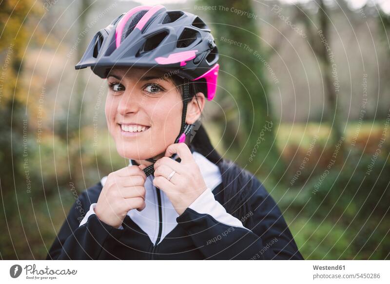 Porträt einer lächelnden Frau, die einen Fahrradhelm aufsetzt Mountainbiking mountainbiken MTB aufsetzen Radhelm Fahrradhelme weiblich Frauen Radsport Sport