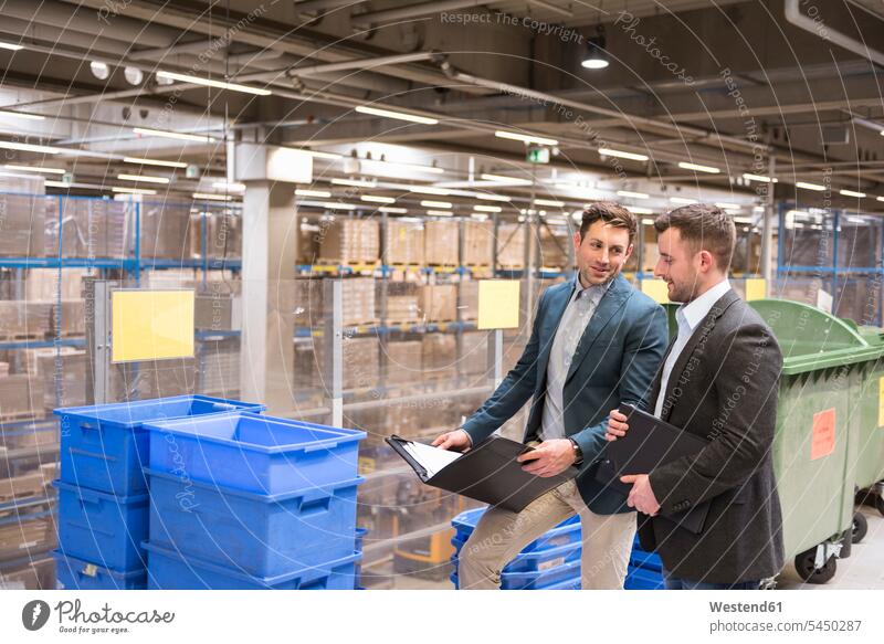 Zwei Geschäftsleute mit Dokumenten im Gespräch im Fabriklager sprechen reden Mann Männer männlich arbeiten Arbeit Kollegen Arbeitskollegen lächeln Lagerhalle