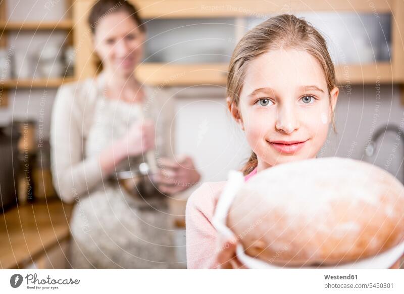 Mädchen hält Brot in der Küche mit der Mutter im Hintergrund Tochter Töchter Brote weiblich Küchen Kind Kinder Familie Familien Mensch Menschen Leute People