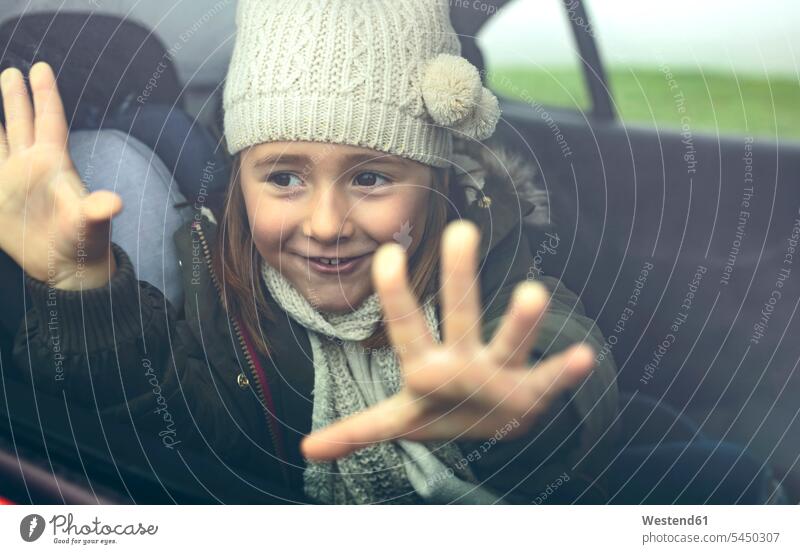 Porträt eines glücklichen kleinen Mädchens mit Wollmütze, das seine Finger auf das Autofenster legt lächeln weiblich Hand Hände Wagen PKWs Automobil Autos