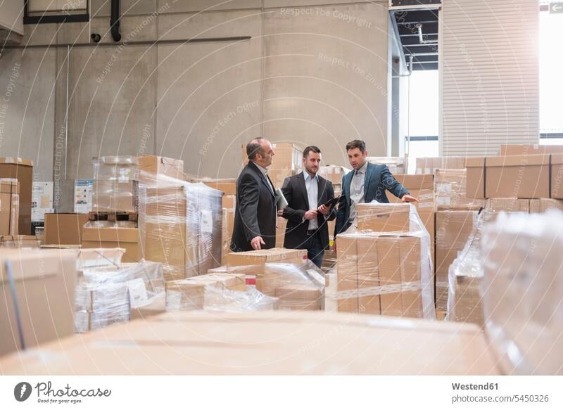 Drei Männer im Fabriklager, umgeben von Pappkartons arbeiten Arbeit Mann männlich Kollegen Arbeitskollegen Geschäftsmann Businessmann Businessmänner