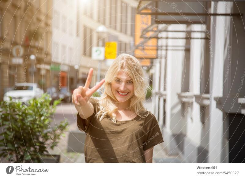 Porträt einer glücklichen blonden Frau mit Siegeszeichen Victory-Zeichen V Zeichen Victory Zeichen Portrait Porträts Portraits weiblich Frauen Handzeichen