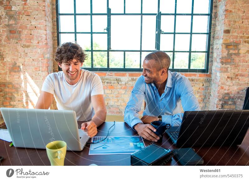 Zwei junge Geschäftsleute arbeiten in einem Arbeitsraum zusammen und benutzen Laptops Planung Pläne planen Geschäftspersonen Start-up Startups Start ups