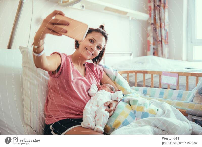 Mutter macht ein Selfie mit ihrem neugeborenen Baby im Krankenhausbett Mami Mutti Mütter Mama Selfies Eltern Familie Familien Mensch Menschen Leute People