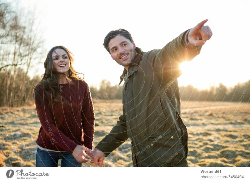 Junges Paar macht einen Spaziergang in der Abendsonne Pärchen Paare Partnerschaft herbstlich zeigen mit dem Finger zeigen deuten Sonnenuntergang