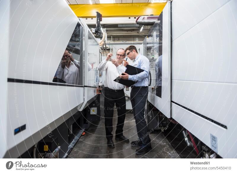 Zwei Männer unterhalten sich zwischen Maschinen in der Fabrikhalle Fabriken Mann männlich Kollegen Arbeitskollegen sprechen reden Erwachsener erwachsen Mensch