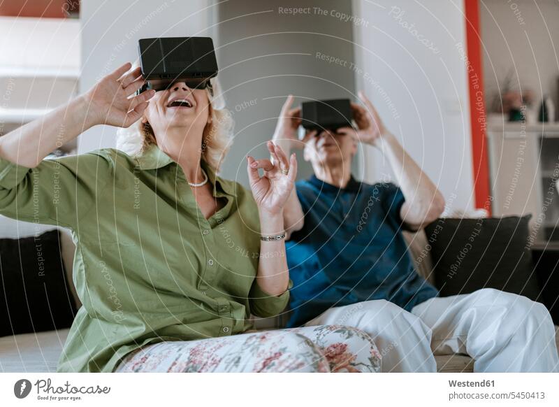 Glückliches älteres Ehepaar zu Hause, das mit einer VR-Brille auf der Couch sitzt Sofa Couches Liege Sofas Paar Pärchen Paare Partnerschaft