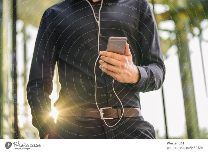 Geschäftsmann hält ein Smartphone mit angeschlossenen Kopfhörern Handy Mobiltelefon Handies Handys Mobiltelefone Ohrhörer Mann Männer männlich Businessmann
