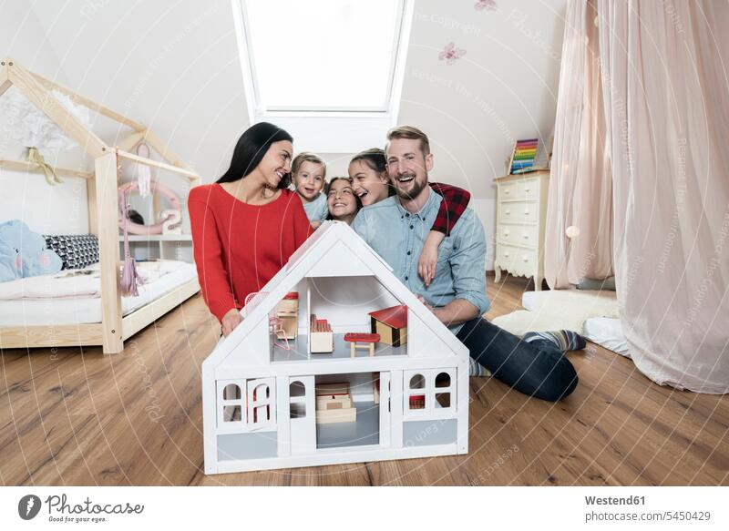 Glückliche Familie mit drei Töchtern, die hinter dem Puppenhaus in der Kinderkrippe sitzen Tochter Spaß Spass Späße spassig Spässe spaßig lachen Familien