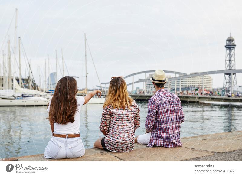 Spanien, Barcelona, drei Touristen sitzen auf einem Pier in der Stadt Freunde Landungssteg Piers Tourismus Freundschaft Kameradschaft Ufer Urban städtisch