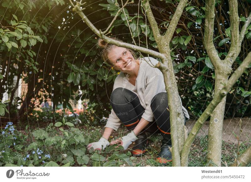 Lächelnde junge Frau räumt Unkraut im Garten Gärten Gaerten Unkraut jäten Unkraut entfernen weiblich Frauen Erwachsener erwachsen Mensch Menschen Leute People