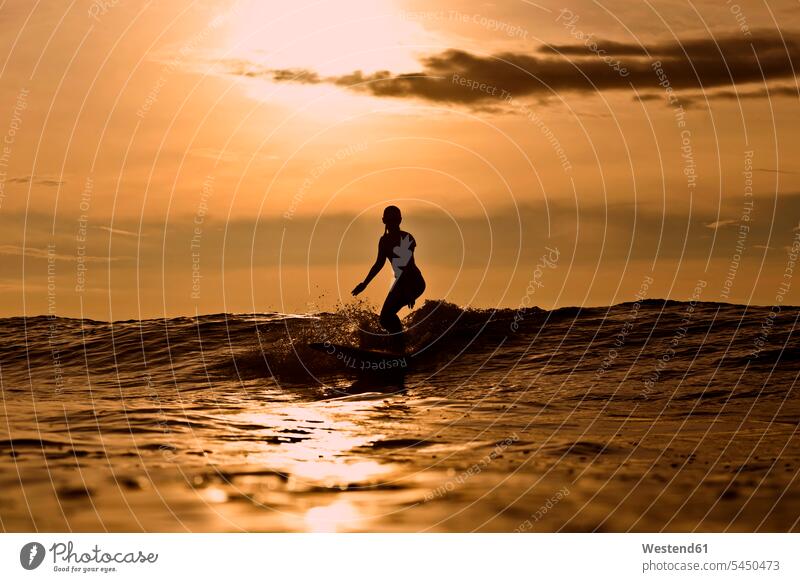 Indonesien, Bali, Silhouette einer Frau, die bei Sonnenuntergang surft Meer Meere Welle Wellen Surfen Surfing Wellenreiten weiblich Frauen Gewässer Wasser
