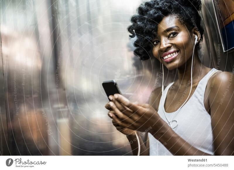 Porträt einer glücklichen Frau mit Handy und Kopfhörern in der U-Bahn Smartphone iPhone Smartphones weiblich Frauen Portrait Porträts Portraits Mobiltelefon