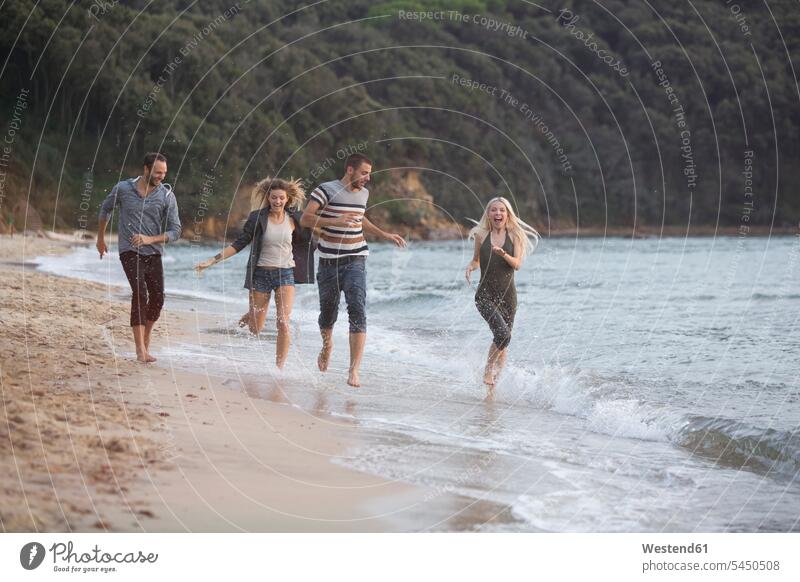 Vier glückliche Freunde laufen am Strand Spaß Spass Späße spassig Spässe spaßig Glück glücklich sein glücklichsein lachen rennen Freundschaft Kameradschaft