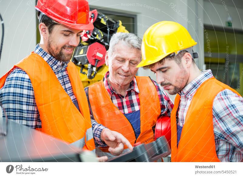 Drei Männer in der Fabrik im Gespräch mit einem Industrieroboter im Hintergrund Fabriken arbeiten Arbeit Roboter industriell Gewerbe Industrien Beruf