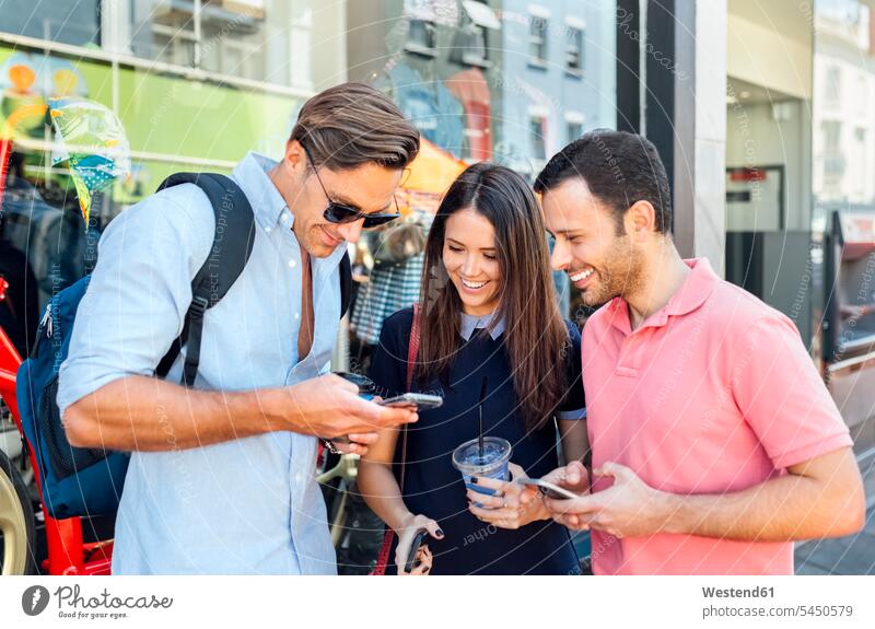Großbritannien, London, Portobello Road, drei lächelnde Freunde beim Blick auf das Handy Smartphone iPhone Smartphones Mobiltelefon Handies Handys Mobiltelefone