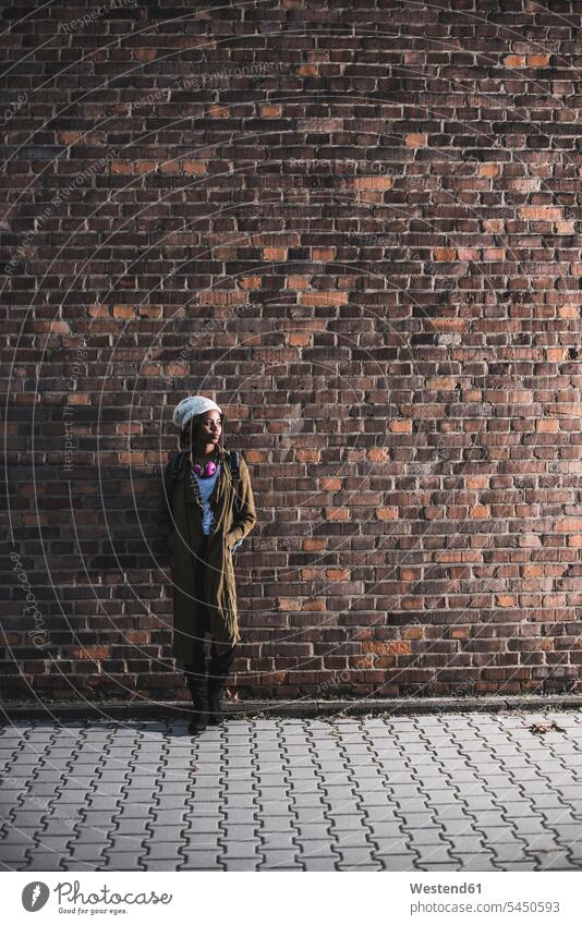 Junge Frau steht vor einer Ziegelmauer weiblich Frauen Erwachsener erwachsen Mensch Menschen Leute People Personen Kopfhörer Kopfhoerer Backsteinwand
