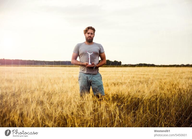 Mann steht im Getreidefeld und hält Miniatur-Windturbine stehen stehend Windrad Windturbinen Windräder Männer männlich halten Feld Felder Kornfeld