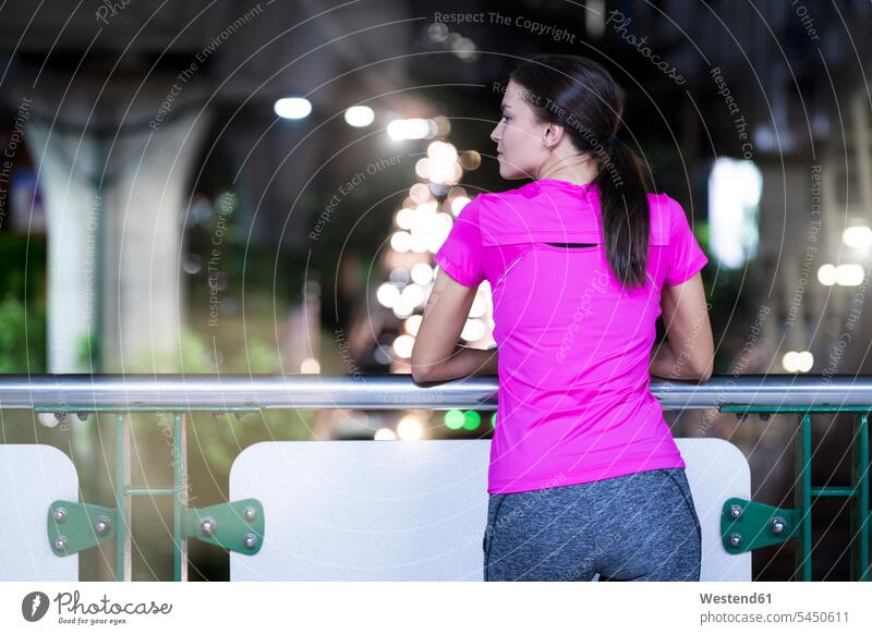 Junge Frau im rosa Sporthemd beobachtet nachts die Lichter der Stadt junge Frau junge Frauen trainieren Joggerin Joggerinnen weiblich Erwachsener erwachsen