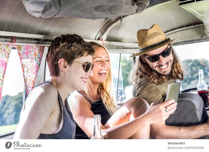 Glückliche Freunde im Transporter beim Blick auf das Smartphone Kleinbus Kleinbusse lachen Spaß Spass Späße spassig Spässe spaßig Handy Mobiltelefon Handies