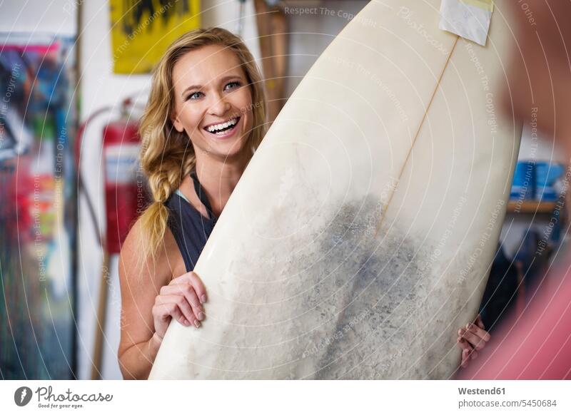 Surfbrett-Shaper-Workshop, weibliche Angestellte lächelt mit Surfbrett lachen Surfbretter surfboard surfboards Frau Frauen positiv Emotion Gefühl Empfindung