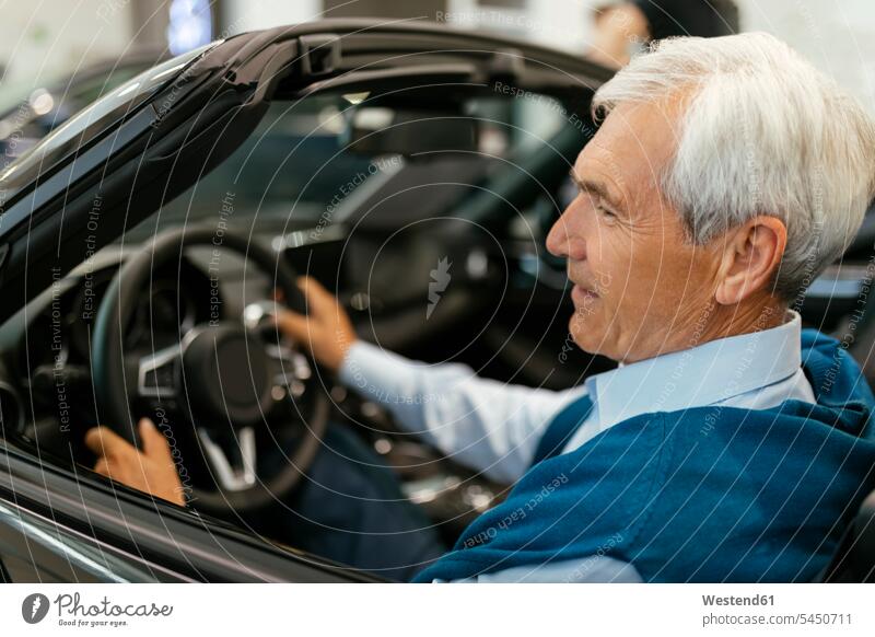 Leitender Mann testet Cabriolet im Autohaus Wagen PKWs Automobil Autos aussuchen auswählen Kunde Kunden Kundschaft Probefahrt kaufen Kauf Autohäuser Autohaeuser