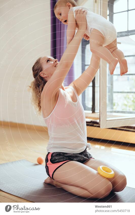 Mutter hält ihr Baby hoch, während sie auf einer Yogamatte trainiert trainieren Spaß Spass Späße spassig Spässe spaßig Mami Mutti Mütter Mama Yoga-Übungen