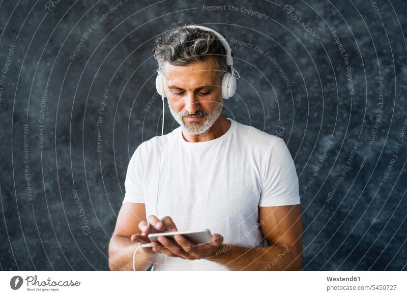 Porträt eines reifen Mannes, der ein Smartphone benutzt und Kopfhörer trägt reifer Mann reife Männer Musik iPhone Smartphones Anruf telefonieren anrufen