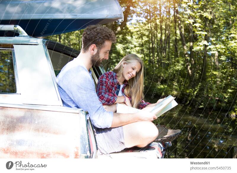 Lächelndes junges Paar mit Karte und Kanu im Auto an einem Bach Landkarte Landkarten Bäche Baeche Wald Forst Wälder lächeln Wagen PKWs Automobil Autos Kanus