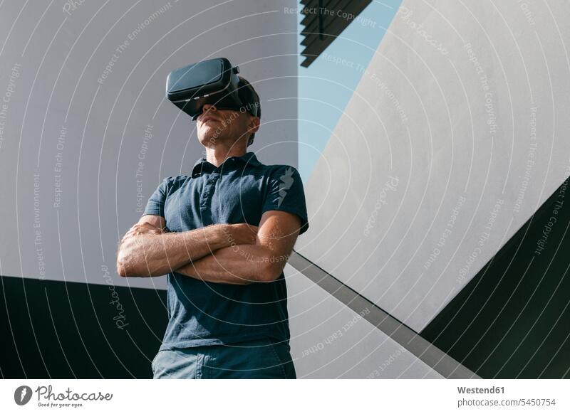 Reifer Mann mit VR-Brille steht zwischen Wänden moderner Architektur Baukunst Mauer Mauern Virtuelle Realität Virtuelle Realitaet Männer männlich Brillen stehen
