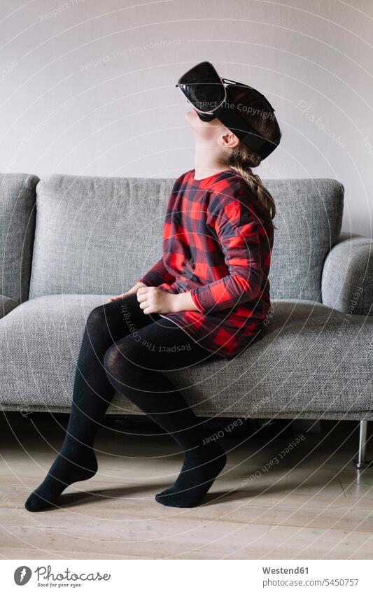 Mädchen sitzt auf der Couch im Wohnzimmer und benutzt eine Virtual-Reality-Brille Sofa Couches Liege Sofas Wohnraum Wohnung Wohnen Wohnräume Wohnungen benutzen