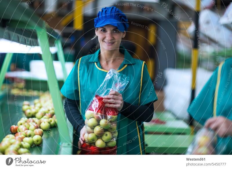 Porträt einer lächelnden Frau, die in der Fabrik Äpfel in Plastiktüten hält weiblich Frauen Fabrikgebäude Fabrikgebaeude Fabriken arbeiten Arbeit Apfel Aepfel