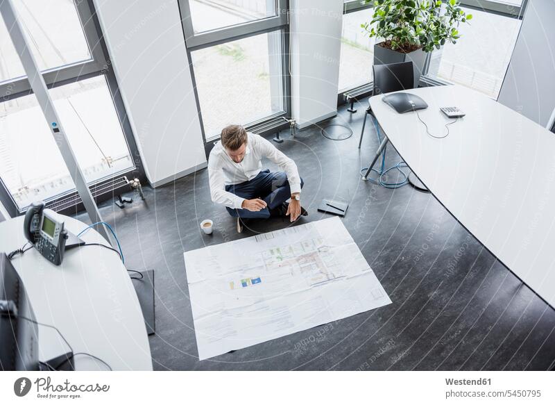 Geschäftsmann sitzt auf dem Boden seines Büros und betrachtet Bauplan Businessmann Businessmänner Geschäftsmänner Office Geschäftsleute Geschäftspersonen