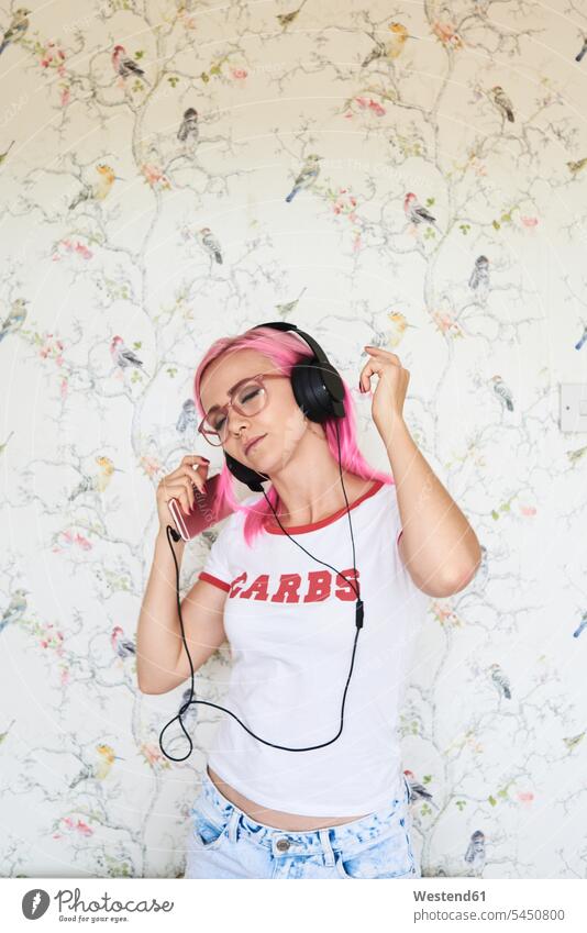 Enthusiastische junge Frau mit rosa Haaren, die zu Hause Musik hört Kopfhörer Kopfhoerer Handy Mobiltelefon Handies Handys Mobiltelefone tanzen tanzend hören