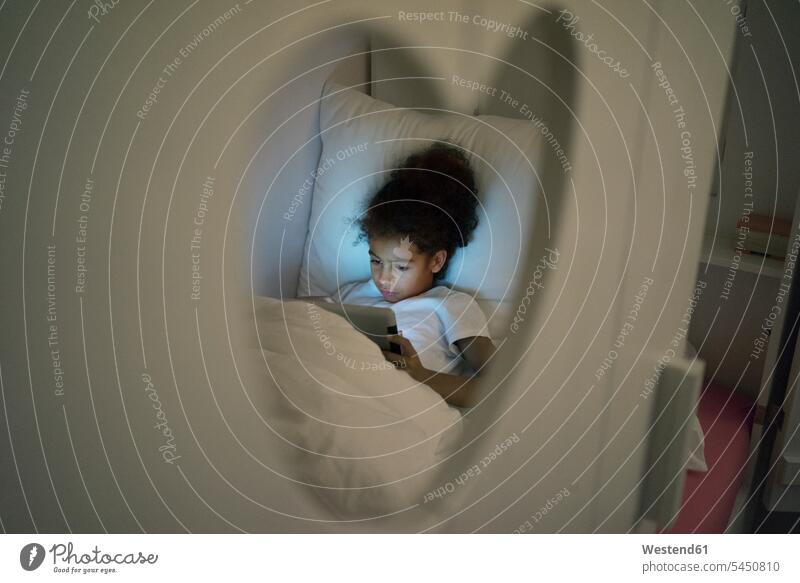 Kleines Mädchen sitzt im dunklen Kinderzimmer und schaut auf ein digitales Tablet dunkel spielen lesen Lektüre sitzen sitzend Zimmer Raum Räume Komfortabel