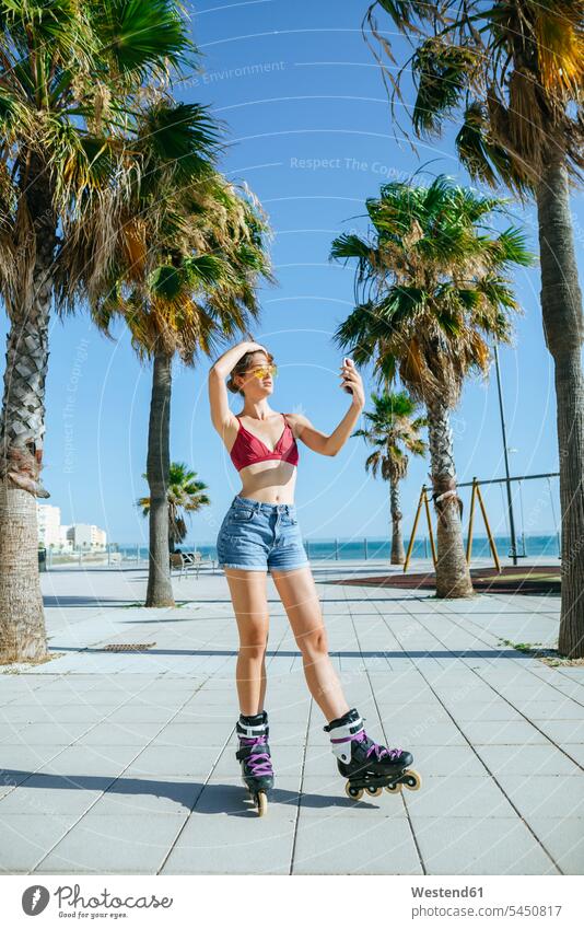 Junge Frau auf Inline-Skates macht ein Selfie auf der Strandpromenade Inlineskates Inline skates inline skate Inliner Handy Mobiltelefon Handies Handys