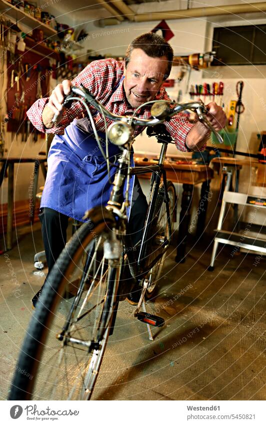Älterer Mann überprüft Fahrrad in seiner Werkstatt Bikes Fahrräder Räder Rad Werkstätte Werkstaette Werkstaetten Werkstätten Senior ältere Männer älterer Mann