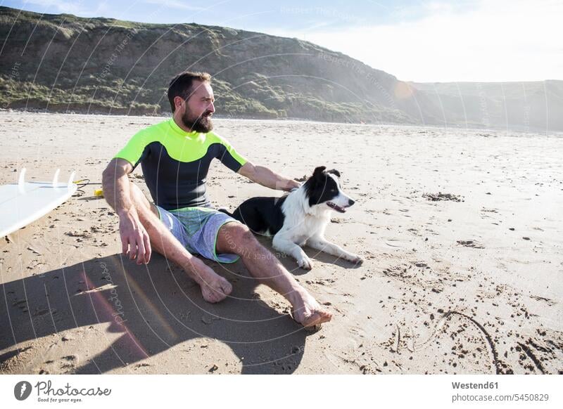 Mann mit Hund und Surfbrett am Strand Hunde Männer männlich Beach Straende Strände Beaches sitzen sitzend sitzt Surfer Wellenreiter Haustier Haustiere Tier