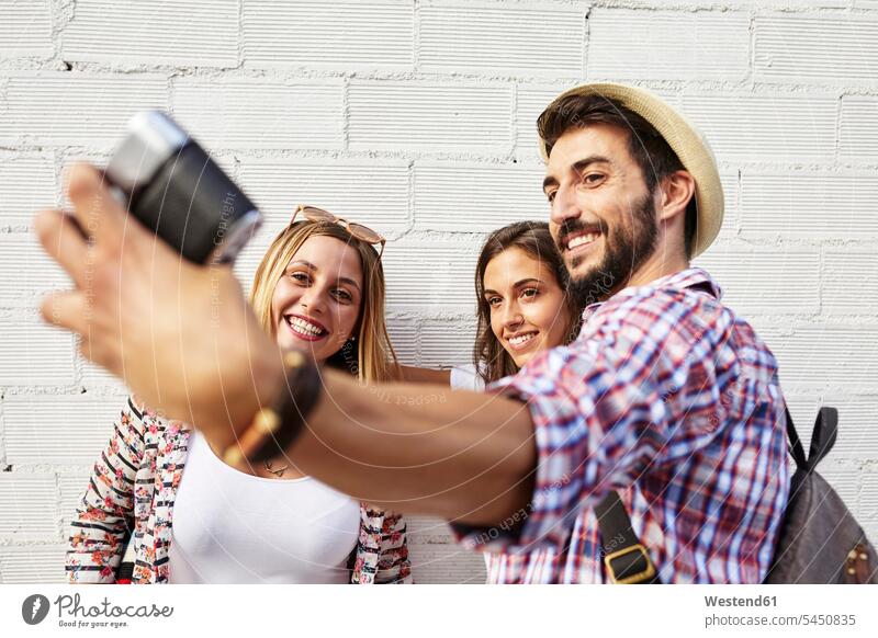 Drei Freunde fotografieren an der weißen Wand lächeln Fotoapparat Kamera Fotokamera Selfie Selfies Freundschaft Kameradschaft Wände Waende Gemeinsam Zusammen