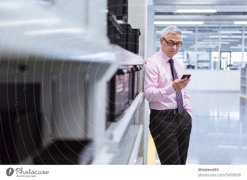 Manager in der Fabrikhalle einer Fabrik mit Smartphone stehen stehend steht iPhone Smartphones lesen Lektüre Geschäftsmann Businessmann Businessmänner