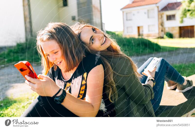 Zwei glückliche Mädchen benutzen ihre Smartphones im Freien weiblich Schwester Schwestern Glück glücklich sein glücklichsein lachen Handy Mobiltelefon Handies