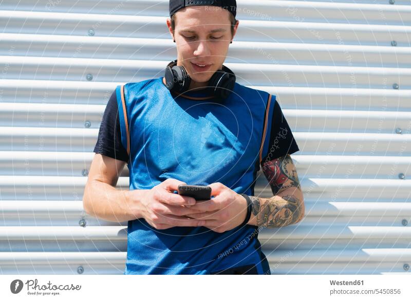 Tätowierter junger Mann mit Kopfhörern schaut auf Handy Männer männlich Smartphone iPhone Smartphones Erwachsener erwachsen Mensch Menschen Leute People