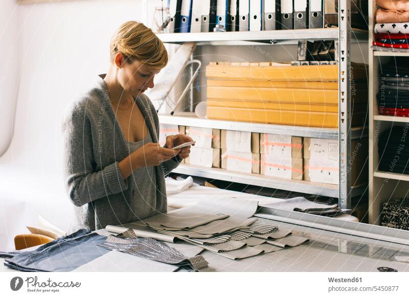 Modedesignerin benutzt Handy im Atelier arbeiten Arbeit Schneiderin Schneiderinnen Frau weiblich Frauen SMS Textnachricht Mobiltelefon Handies Handys