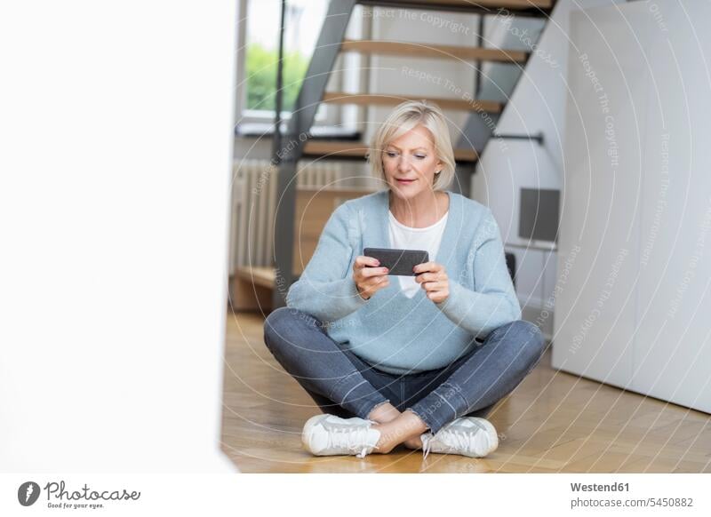 Porträt einer älteren Frau, die zu Hause auf dem Boden sitzt und ein Smartphone benutzt iPhone Smartphones Portrait Porträts Portraits weiblich Frauen sitzen