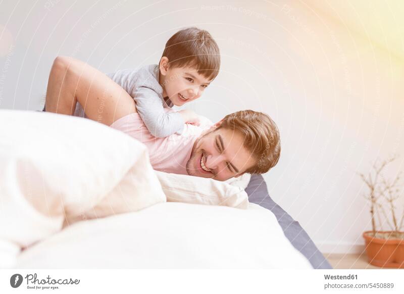Glückliche Vater und Sohn spielen im Bett Betten Papas Väter Vati Vatis Papis Söhne lächeln Eltern Familie Familien Mensch Menschen Leute People Personen Kind