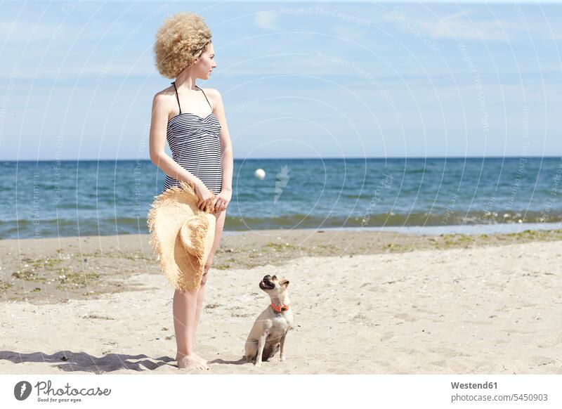 Junge Frau im Badeanzug mit Strohhut und Hund am Strand Hunde weiblich Frauen Beach Straende Strände Beaches Haustier Haustiere Tier Tierwelt Tiere Erwachsener