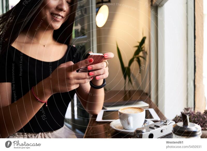 Lächelnde asiatische Frau plaudert mit ihrem Telefon in einem Café neben dem Fenster Smartphone iPhone Smartphones Asiatin Asiatinnen asiatisches asiatischer