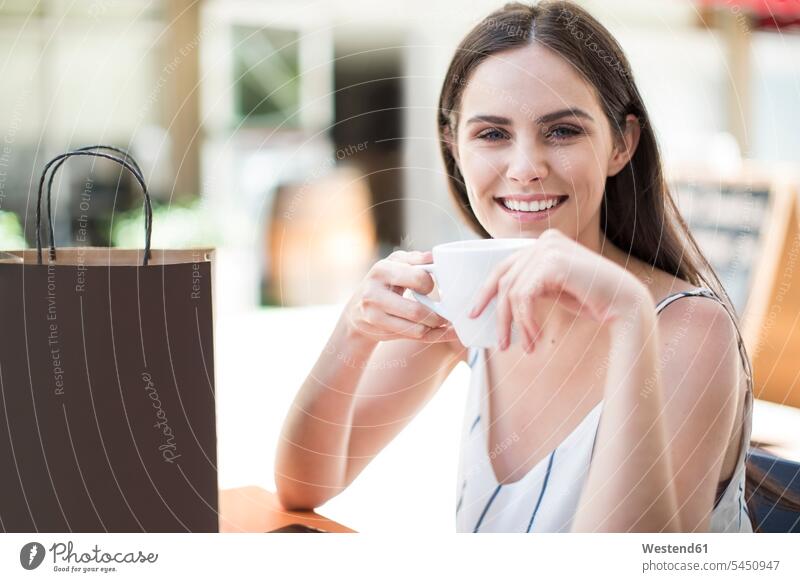 Lächelnde Frau mit Einkaufstasche genießt Kaffee im Café Cafe Kaffeehaus Bistro Cafes Cafés Kaffeehäuser glücklich Glück glücklich sein glücklichsein lächeln